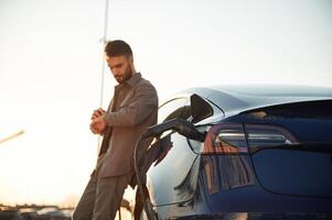 Charging process,. Man is standing near his electric car outdoors photo