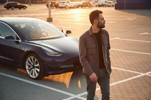 Handsom,e man ,is standing near his electric car outdoors photo