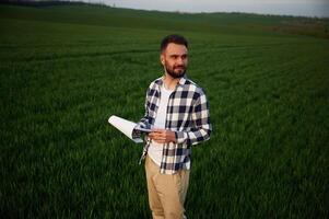 Front view. Standing and, holding notepad with document. Handsome young man is on agricultural field photo