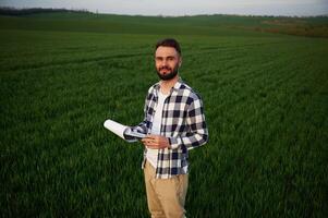 Front ,view. ,Standing, and holding notepad with document. Handsome young man is on agricultural field photo