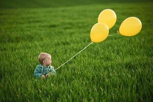 With, yellow balloons in hands. Cute little baby boy is in the agricultural field at daytime photo
