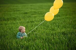 With yellow balloons in hands. Cute little baby boy is in the agricultural field at daytime photo