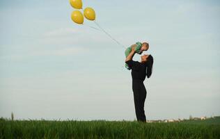Yellow, colored balloons in, hands. Mother with her little baby son is outdoors on the agricultural field photo