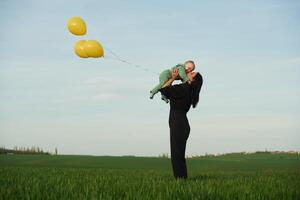 With ,yellow, colored balloons. Mother with her little baby son is outdoors on the agricultural field photo