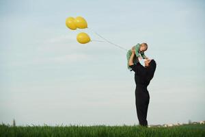 Yellow colored balloons, in ,hands. Mother with her little baby son is outdoors on the agricultural field photo