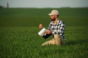 In checkered, shirt ,and with notepad. Handsome young man is on agricultural field photo