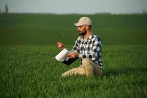 In checkered, shirt and with notepad. Handsome young man is on agricultural field photo