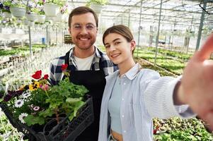 Making selfie, smiling. Florist ,man and woman are working together in bright greenhouse photo