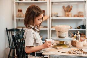 Side, view. Little ,girl is indoors, with ceramic pot in hands photo