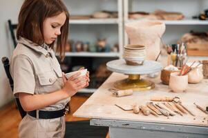 Side view. ,Little girl is indoors with ceramic pot in hands photo