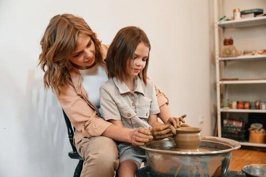Using c,lay to, create,the pot. Mother with little girl learning pottery in the workshop photo