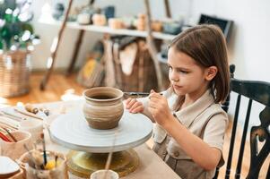 Painting ,the pot by, brush. Little girl is learning how to do pottery in the workshop photo
