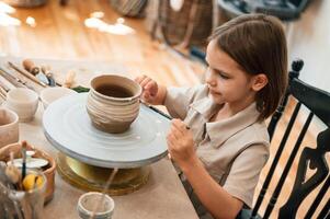 Painting the pot ,by brush. Little girl is learning how to do pottery in the workshop photo