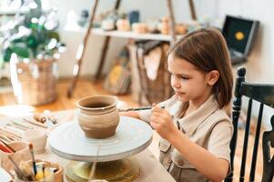 Painting the, pot by brush. Little girl is learning how to do pottery in the workshop photo