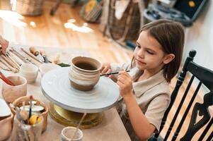 Painting ,the pot by brush. Little girl is learning how to do pottery in the workshop photo