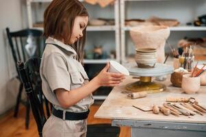 Side view.. Little girl is indoors with ceramic pot in hands photo