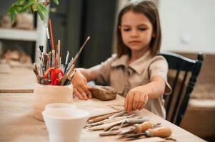 Different ,tools on the table. Little girl is learning how to do pottery in the workshop photo