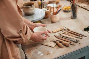 Woman holding ceramic pot in hands. Table with tools. Close up view photo