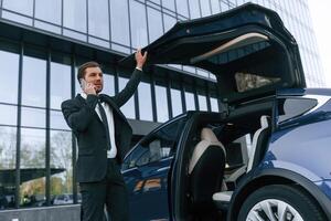 Talking ,by, phone. Businessman is standing near his car outdoors photo