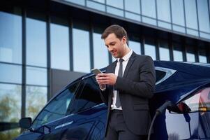 Using smartphone. Businessman ,is standing near his car outdoors photo