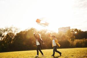 Running together. ..Two kids are playing with kite on the summer field photo