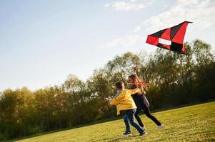 Running together. .Two kids, are playing, with kite on the summer field photo