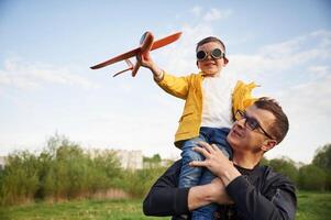 Boy ,is sitting on man's shoulders. Father with his little son playing with toy plane on the field photo
