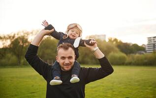 Boy is sitting on man's shoulders., Father with his little son playing with toy plane on the field photo
