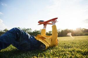 Lying down on ground.. Little boy is playing with toy plane on the summer field photo