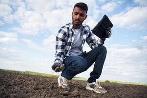 Conception of quality control, with digital tablet. Handsome Indian man is on the agricultural field photo