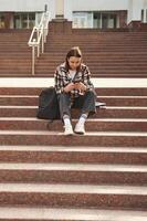 Smartphone in hands.. Young, female student is sitting on the stairs of university photo