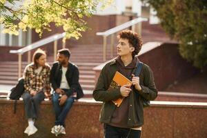 With yellow, colored notepad. Young students in casual clothes are together outdoors photo