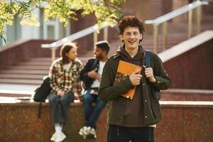 With yellow colored notepad.,. Young students in casual clothes are together outdoors photo