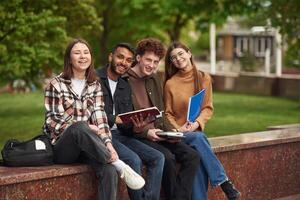 Sitting ,and smiling. Four young, students in casual clothes are together outdoors photo