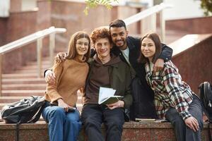 Embracing ,each, other, sitting and smiling. Four young students in casual clothes are together outdoors photo