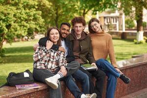 Sitting and smiling,. Four young students in casual clothes are together outdoors photo