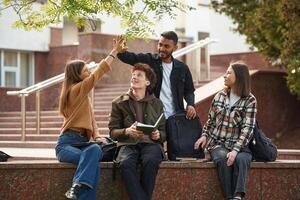 Doing high five. Four, young, students in casual clothes are together outdoors photo