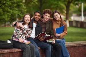 Sitting and smiling. Four young students, in casual clothes are together outdoors photo