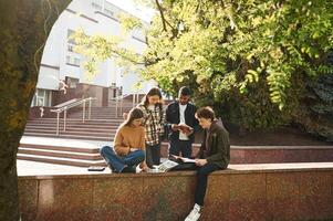 Tree with green leaves.. Four young students in casual clothes are together outdoors photo