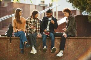 Illuminated by sunlight, ,sitting. Four young students in casual clothes are together outdoors photo