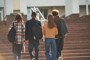 View, from back, walking together. Four young students in casual clothes are outdoors photo