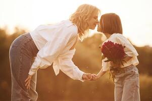 Kid, is holding red flowers. Woman with ,her little daughter are on the summer field together photo