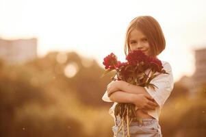 Holding ,,beautiful red flowers. Little girl is on the summer field at daytime photo