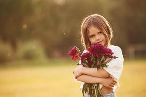 Holding ,beautiful ,red flowers. Little girl is on the summer field at daytime photo