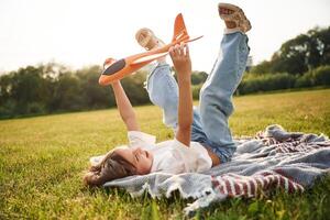Laying, down ,on the ground. Happy little girl is playing with toy plane outdoors photo