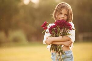 Holding beautiful red flowers.. Little girl is on the summer field at daytime photo