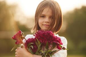 Portrait, standing ,and holding red flowers. Little girl is on the summer field at daytime photo