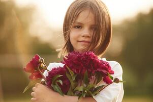 Portrait, standing, and holding red flowers. Little girl is on the summer field at daytime photo