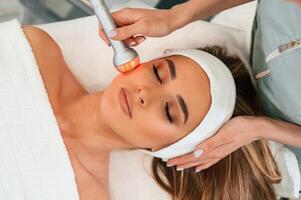 Apparatus for galvanization is used. Woman face getting facial care by beautician hands at spa salon photo