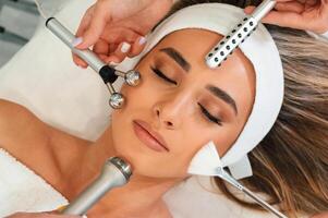 Many, of different ,cosmetitian tools. Woman face getting facial care by beautician hands at spa salon photo